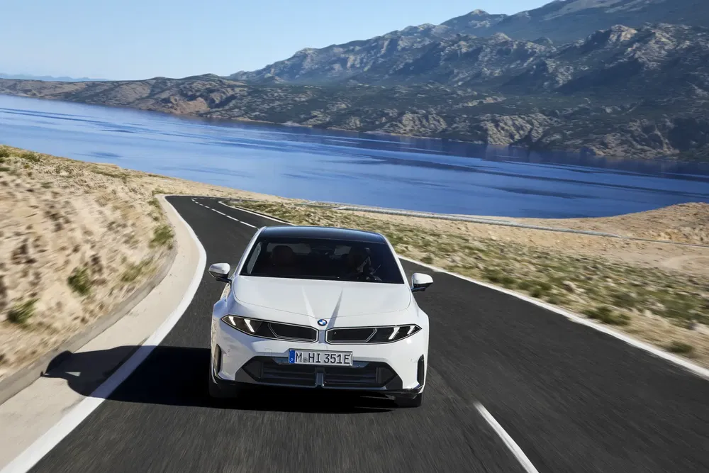 Voiture BMW électrique roulant sur route côtière sinueuse avec vue sur mer et montagnes.