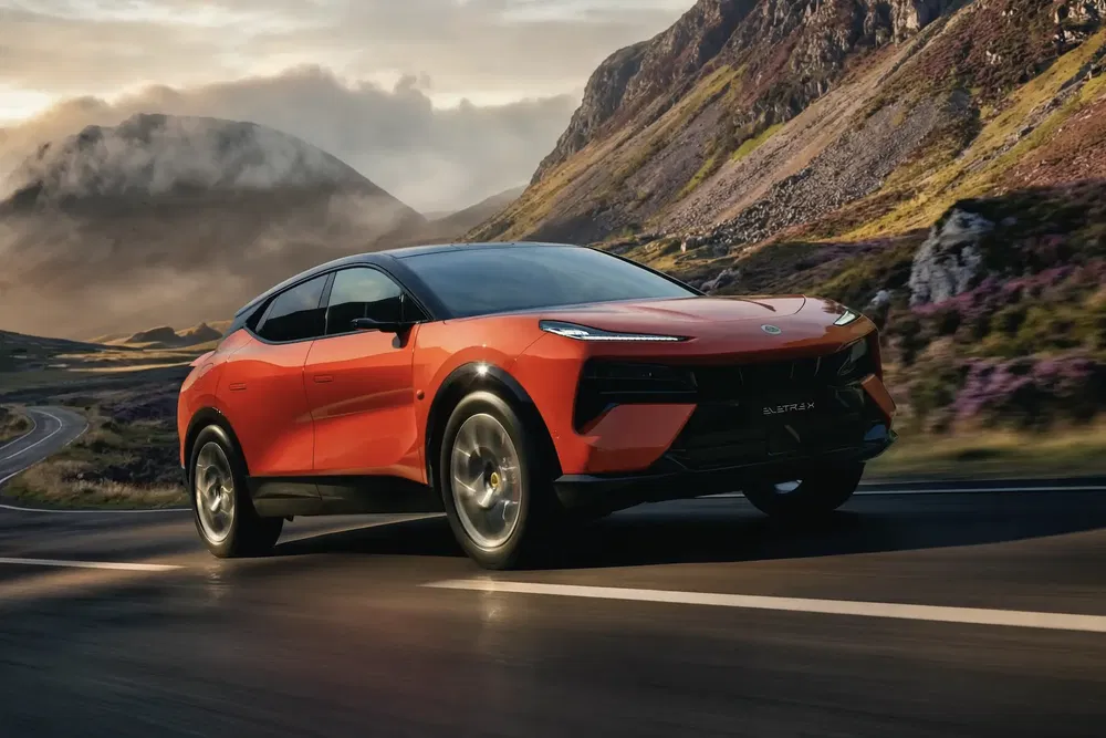 Lotus Eletre orange roulant sur route de campagne pittoresque avec montagnes en arrière-plan.