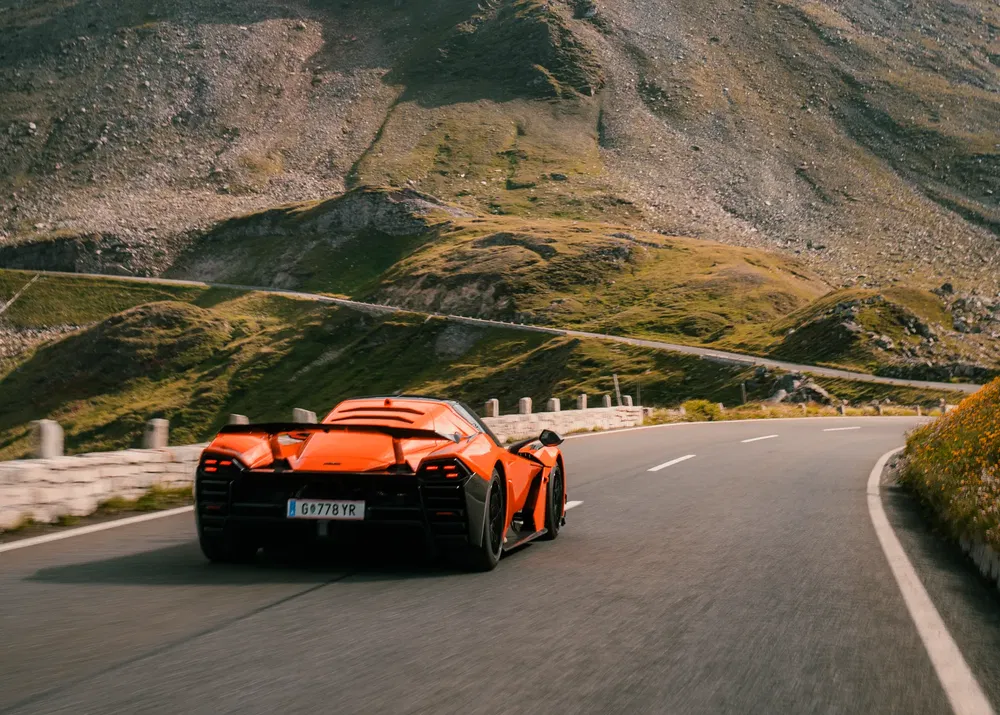 Oranje supercar rijdt snel over een schilderachtige bergweg.