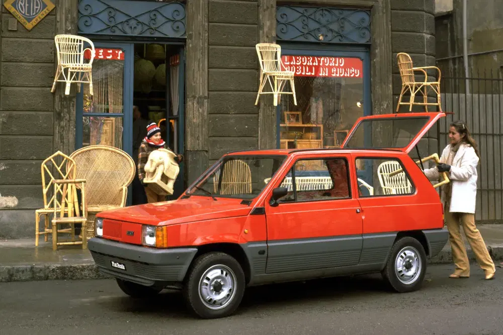 Rode Fiat Panda geparkeerd voor een winkel, geladen met rotan stoelen.