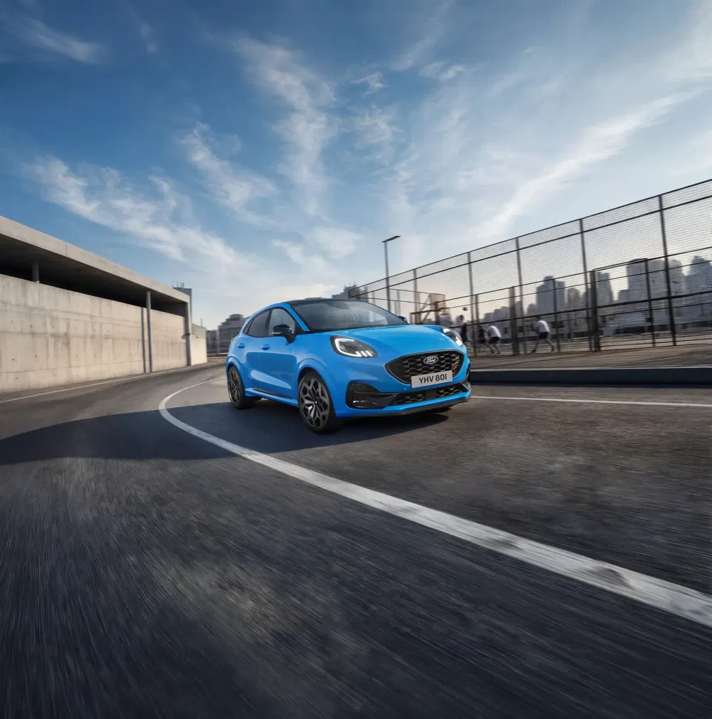 Ford Puma bleu vibrant roulant sur une route urbaine avec des gratte-ciels en arrière-plan.