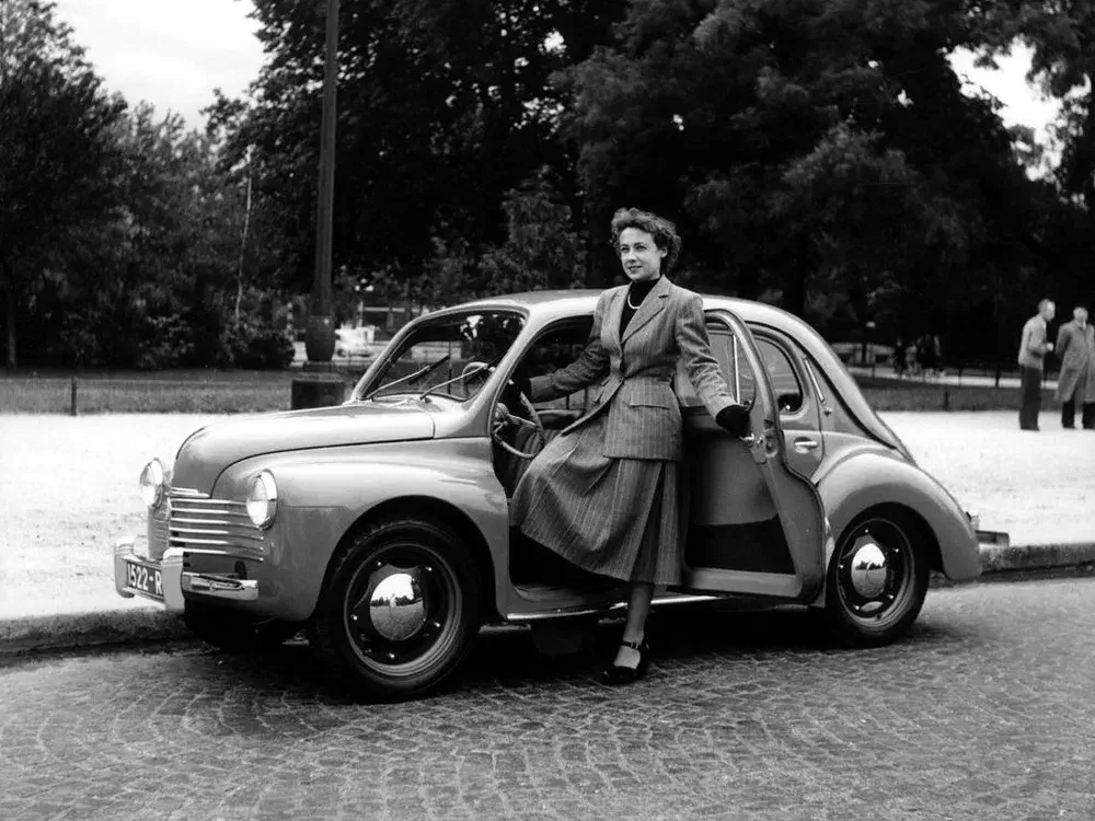 Femme élégante posant avec une Peugeot 203 classique sur route pavée, années 1950.