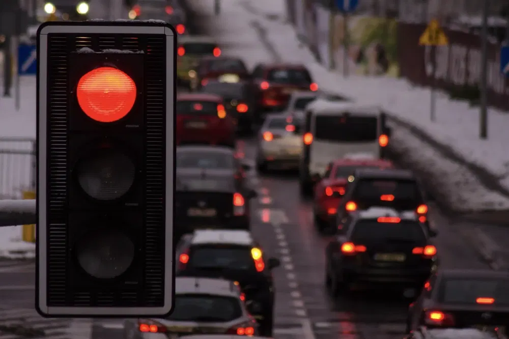 Feu rouge sur une route enneigée avec circulation intense en arrière-plan en hiver.