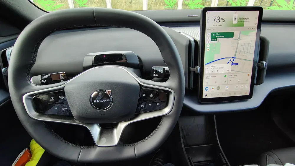 Intérieur d'une Volvo avec volant moderne et grand écran tactile affichant la navigation.