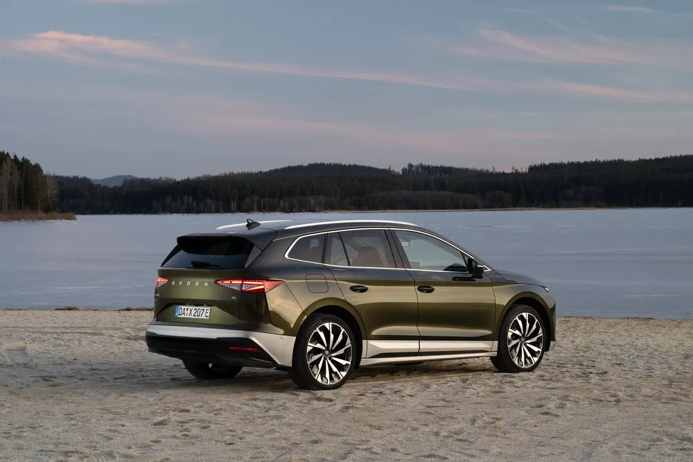 SUV Škoda Enyaq iV vert sur plage, arrière, paysage lac et forêt.