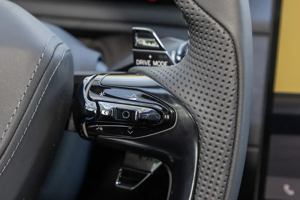 Gros plan sur bouton de commande et volant texturé d'une voiture moderne, mode conduite visible.