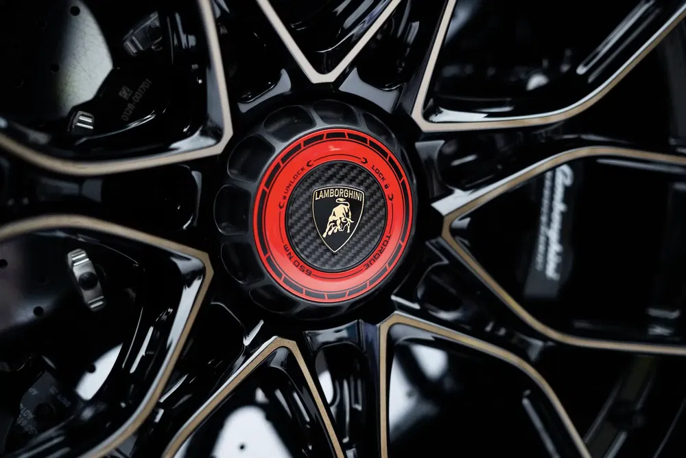 Gros plan sur un moyeu de roue Lamborghini, logo doré sur fond noir et rouge.