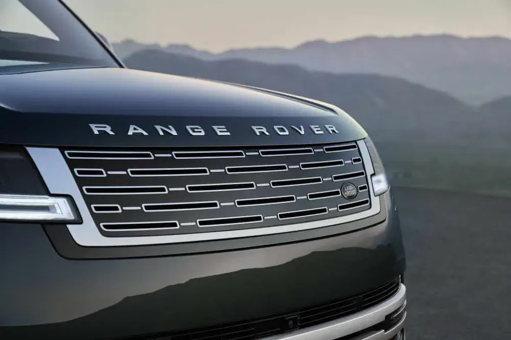 Gros plan sur la calandre avant d'un Range Rover, avec montagnes en arrière-plan.