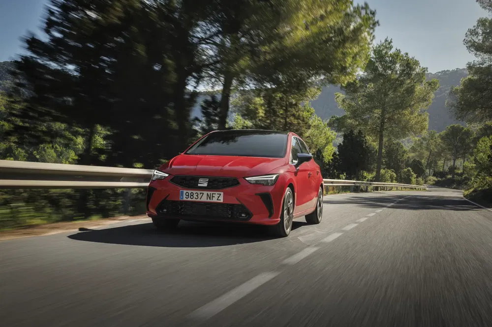 Rode SEAT Ibiza rijdend op een bochtige weg omringd door weelderige bomen.