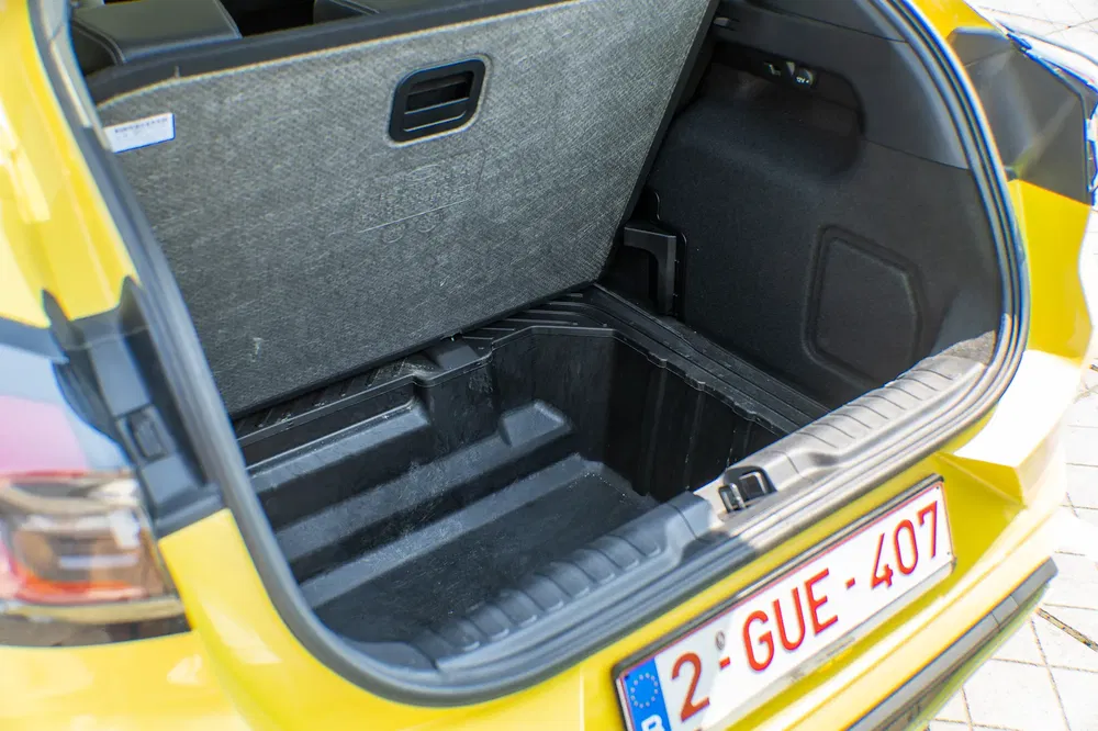 Gele auto kofferbak met ondervloer opbergruimte, Belgische nummerplaat zichtbaar.