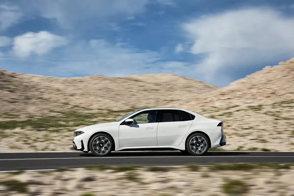 BMW i5 blanc circulant dans un désert, ciel bleu en arrière-plan.