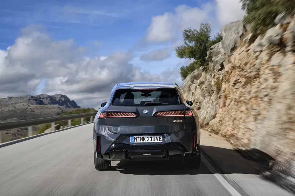 BMW iX en route sinueuse, paysage montagneux en arrière-plan.