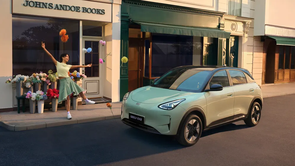 Voiture Geely EX3 verte devant une librairie, femme jongle avec des bouquets de fleurs.