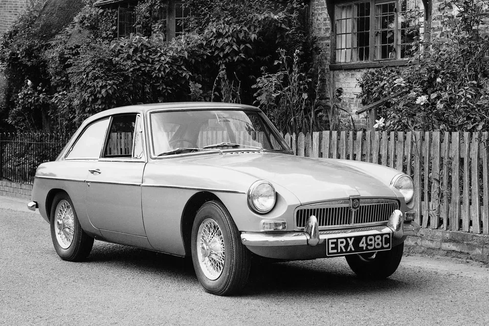 Voiture classique MG B GT des années 1960 garée devant une maison en briques.