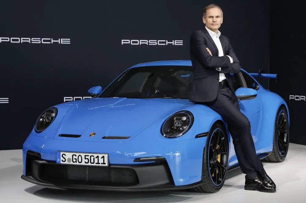 Homme en costume posant avec une Porsche 911 GT3 bleue sur fond noir.