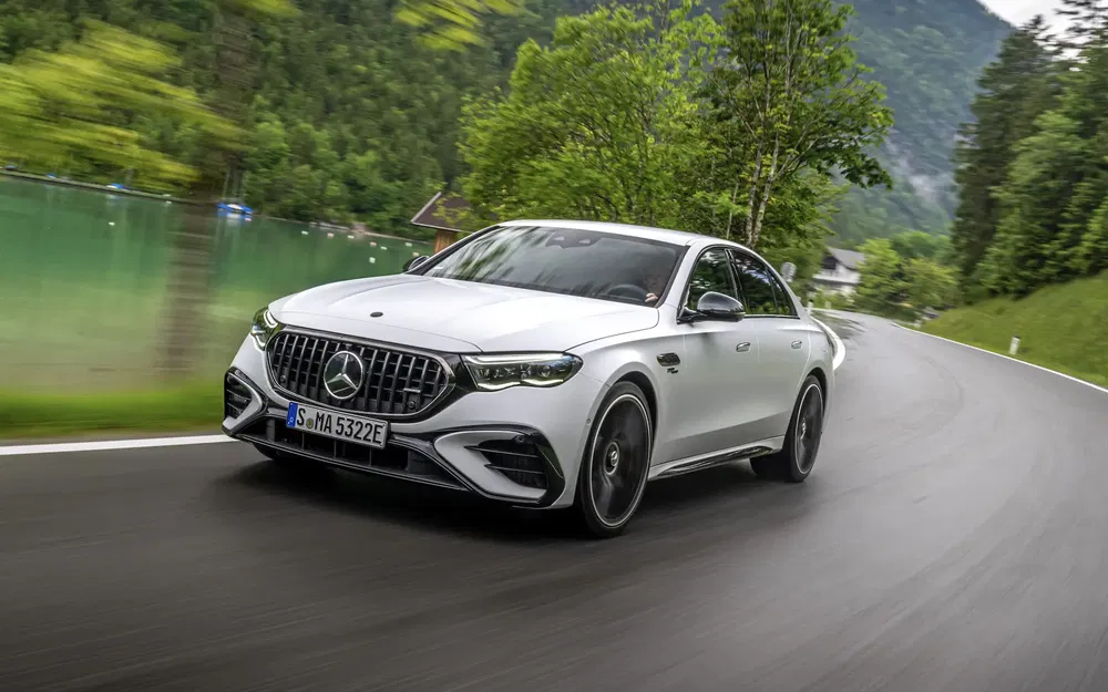 Mercedes E-Class AMG blanche sur route sinueuse en montagne, entourée de verdure luxuriante.
