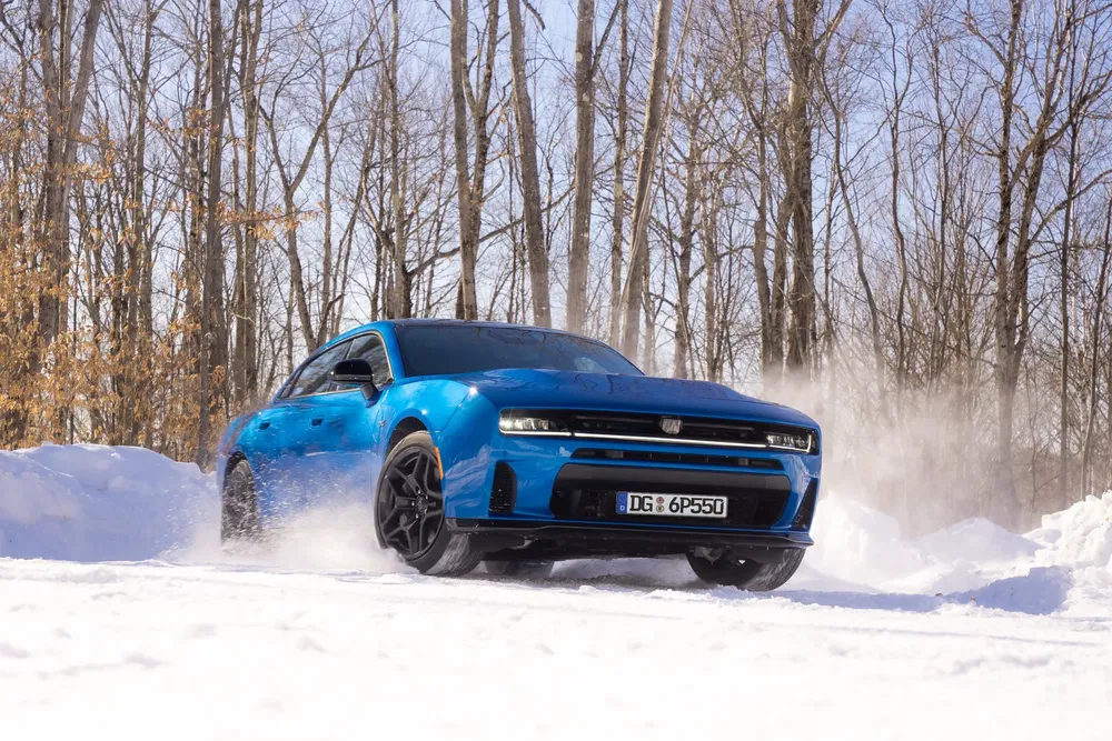 Dodge Charger SRT électrique bleu traverse la neige en forêt hivernale.