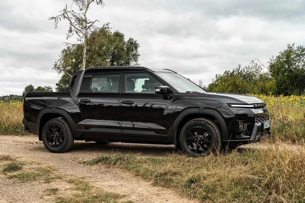 Pick-up noir robuste SsangYong Musso stationné dans un chemin de terre champêtre.