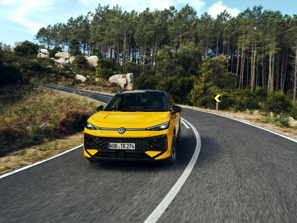 Gele Volkswagen rijdt op kronkelige weg omringd door weelderige groene bossen.