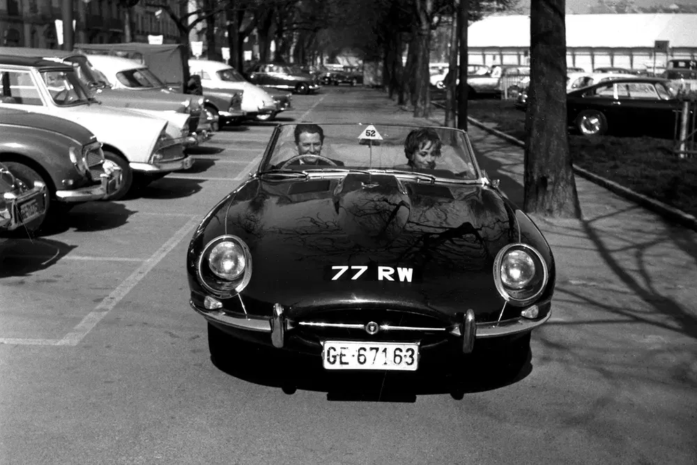 Zwarte Jaguar E-Type cabriolet op straat, klassieke auto's op de achtergrond.