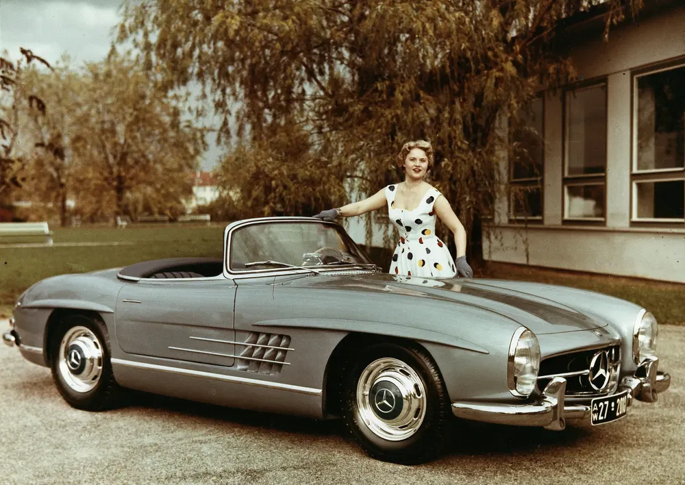 Femme en robe à pois avec Mercedes-Benz 300SL argentée classique, décapotable, paysage automnal.