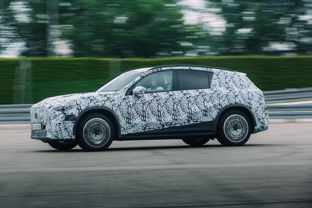 Prototype de SUV camouflage sur piste, testé à grande vitesse, nature floue en arrière-plan.
