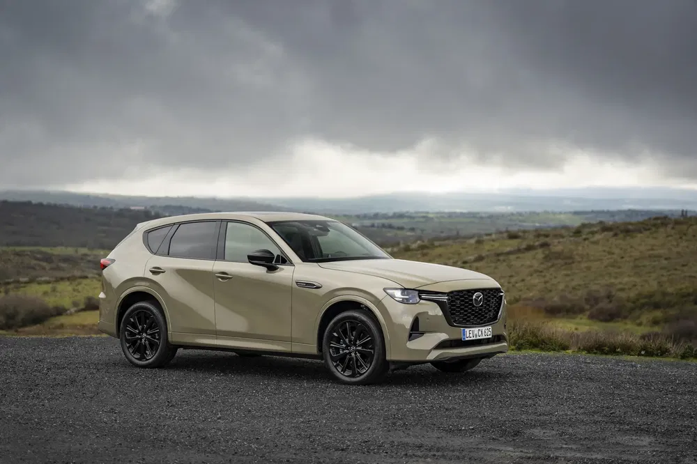 Mazda CX-60 beige stationné sur une route de campagne sous un ciel nuageux.