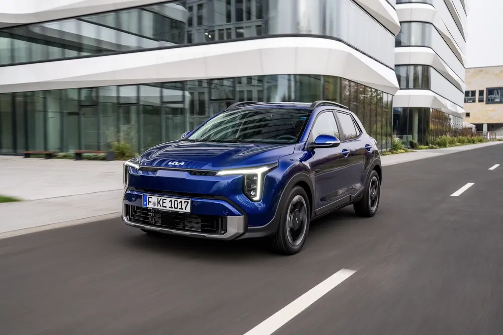 Blauwe elektrische Kia Niro SUV rijdt langs een modern gebouw.