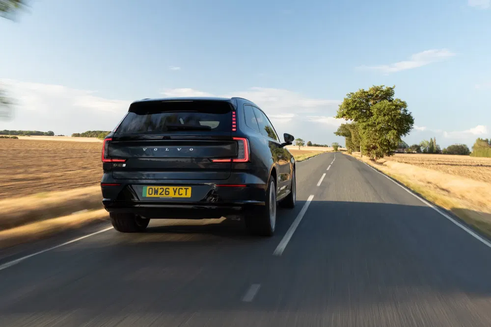 Volvo XC90 roulant sur une route de campagne bordée de champs et d'arbres.