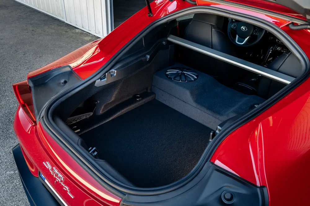 Ruime kofferbak van een rode Toyota met ingebouwde subwoofer en zichtbaar stuur.