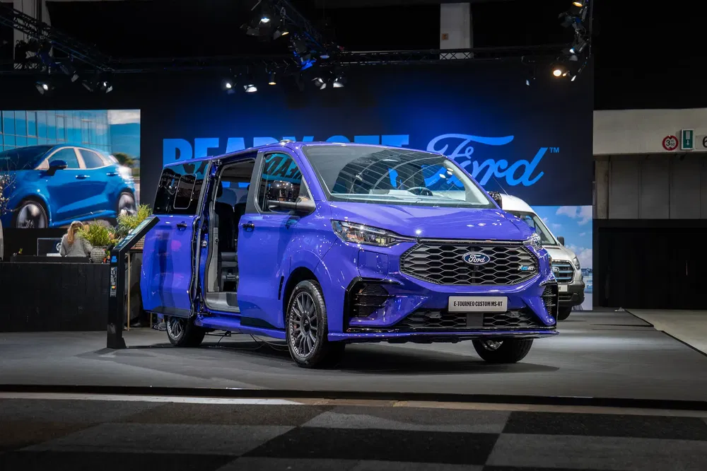 Blauwe Ford E-Tourneo Custom bestelwagen met open schuifdeuren op autobeurs.