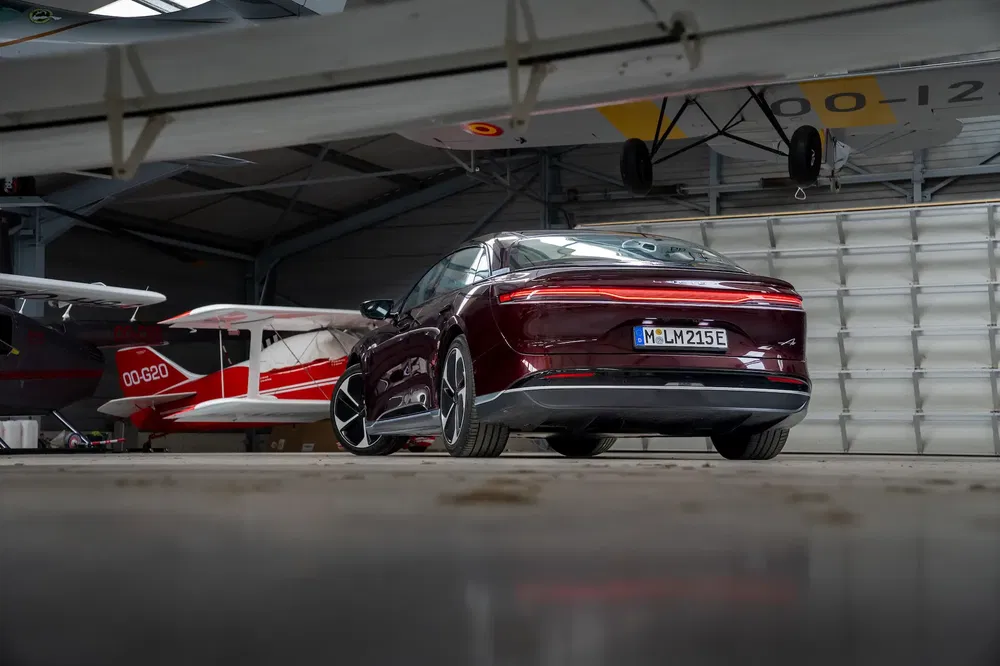 Berline électrique avec avions anciens dans un hangar, couleur bordeaux distinctive en arrière-plan.