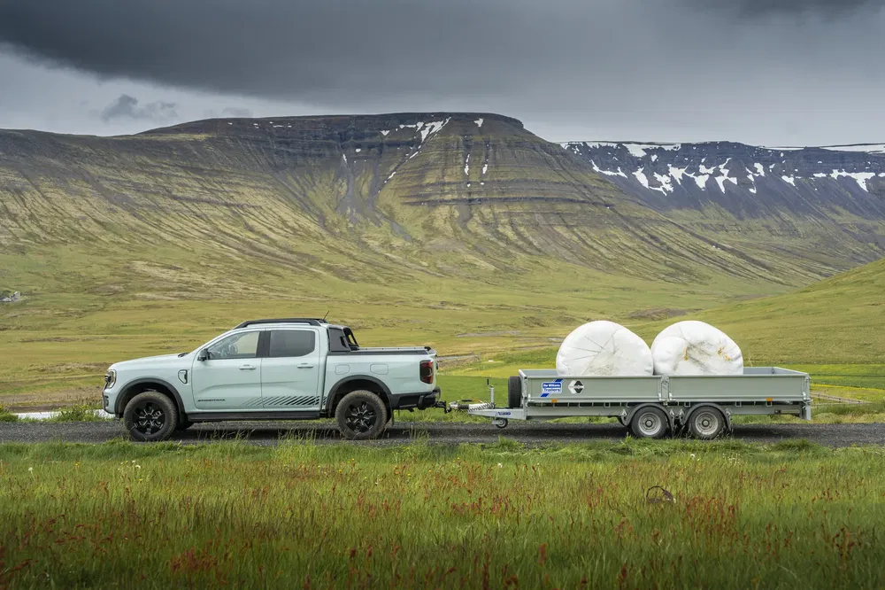 Ford Ranger 2024 pick-up met aanhanger in groene bergachtige omgeving.