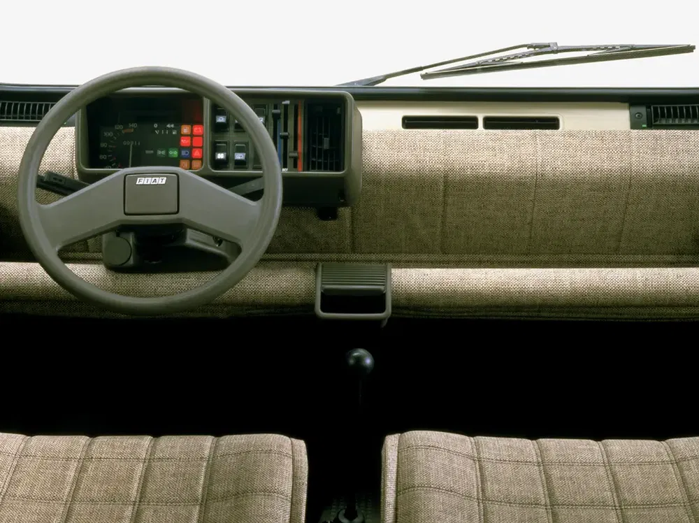 Vintage interieur van Fiat Panda met minimalistisch dashboard en bruine stoffen stoelen.