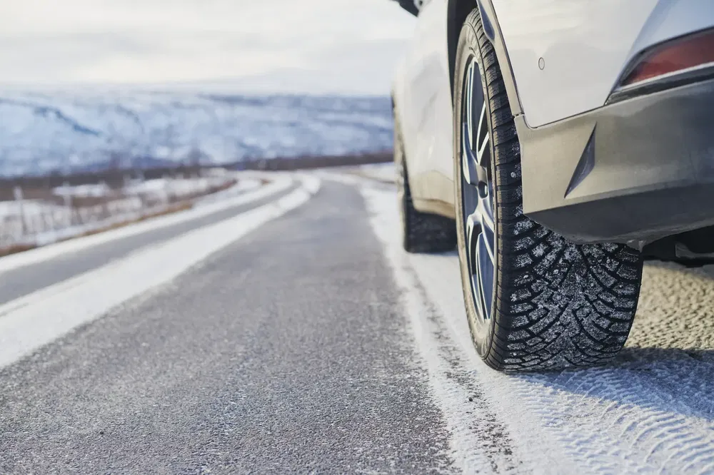 Voiture blanche sur route enneigée, pneus d'hiver en gros plan pour une conduite sécurisée.
