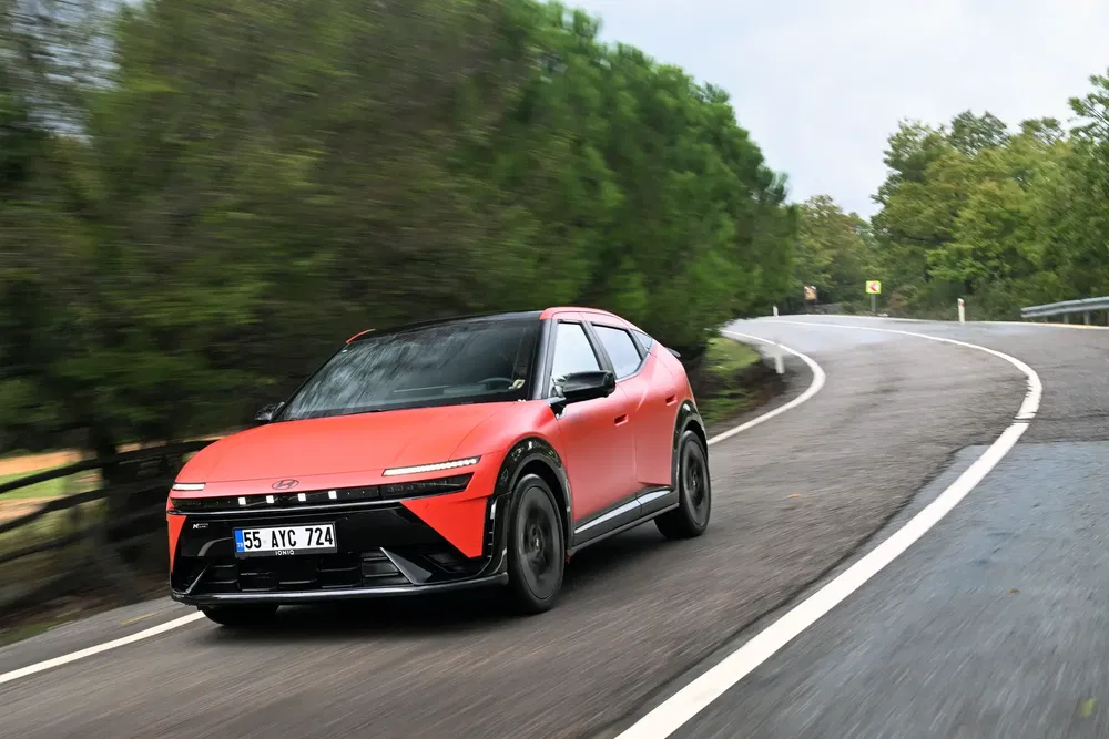 Rode Hyundai Ioniq 5 op kronkelende weg, omgeven door weelderig groen.