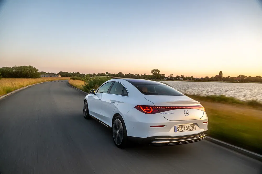 Witte Mercedes-Benz CLA 250e rijdt op schilderachtige weg bij zonsondergang.