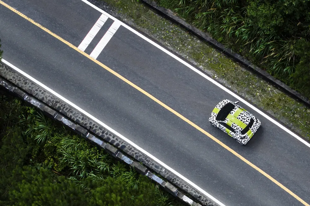 Voiture camouflée sur route sinueuse entourée de verdure, perspective aérienne dynamique.
