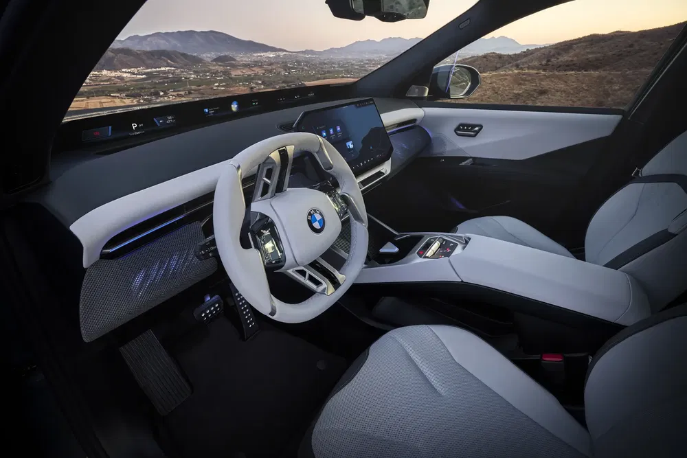 Intérieur futuriste de BMW avec volant innovant et grand écran tactile, vue sur montagnes.