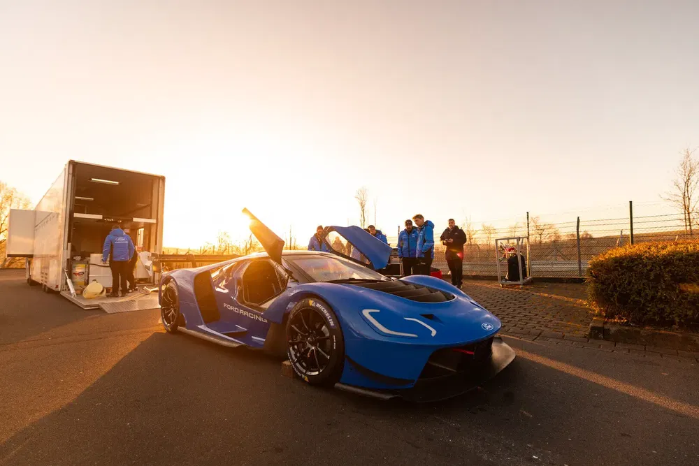 Ford GT bleu avec portes ouvertes au coucher du soleil, équipe d'assistance à proximité.