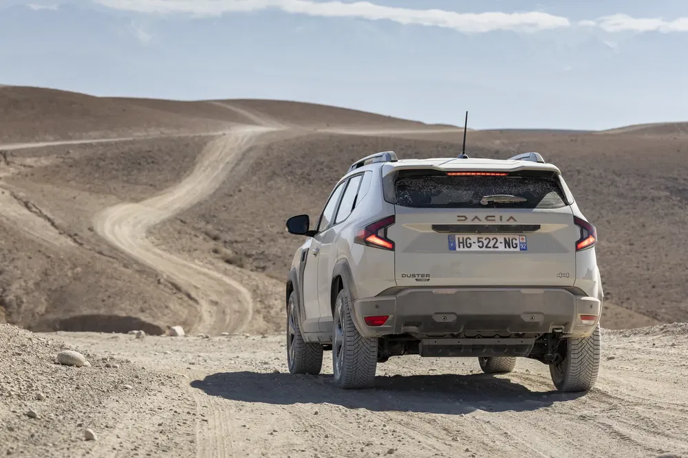 Witte Dacia Duster SUV op stoffige weg in woestijnlandschap onder een heldere hemel.