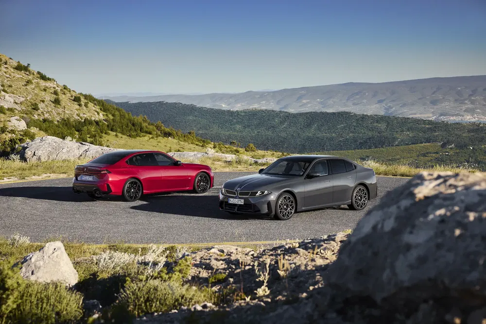 Deux BMW partagées sur une route montagneuse, modèle rouge et gris, paysage panoramique.