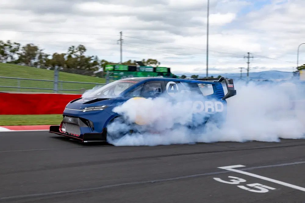 Blauwe Ford racewagen doet burnout op circuit met veel rook.