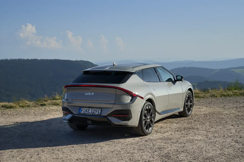 Grijze Kia EV6 geparkeerd, achteraanzicht, voor berglandschap, heldere lucht.