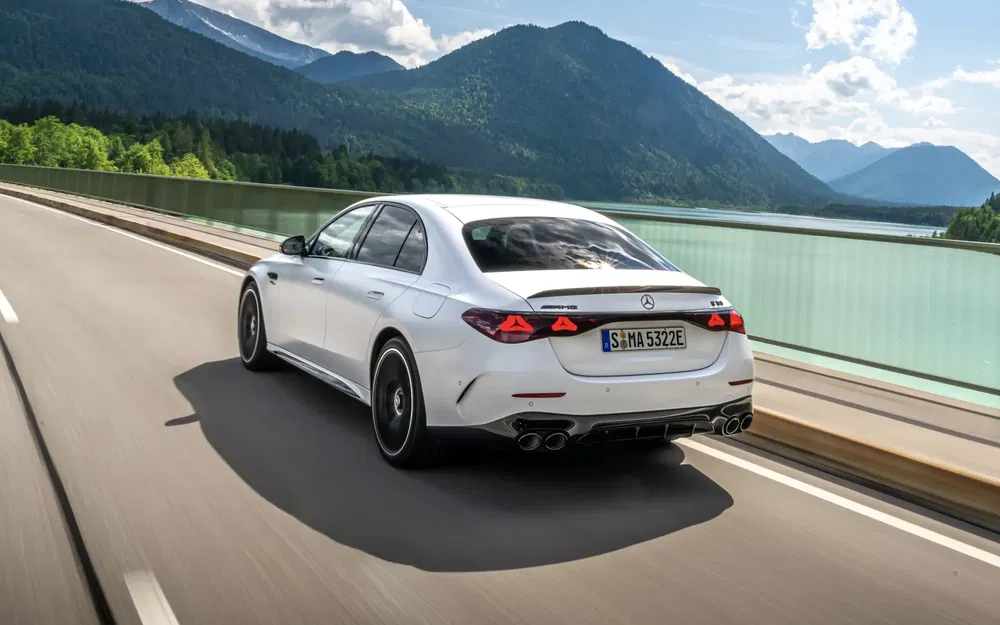 Mercedes classe E berline blanche roulant sur autoroute, montagnes et lac en arrière-plan.
