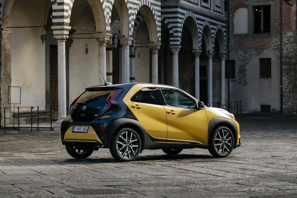 Toyota Aygo X jaune et noir garée dans une cour pavée avec architecture historique.
