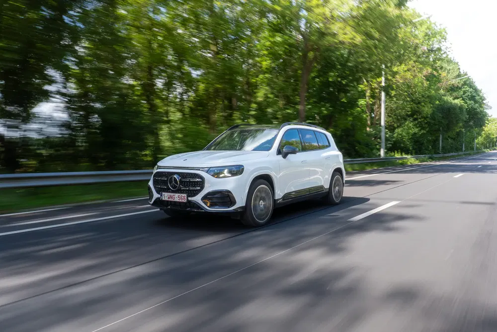 Mercedes-Benz GLC blanc roulant sur une route bordée d'arbres, en pleine nature.