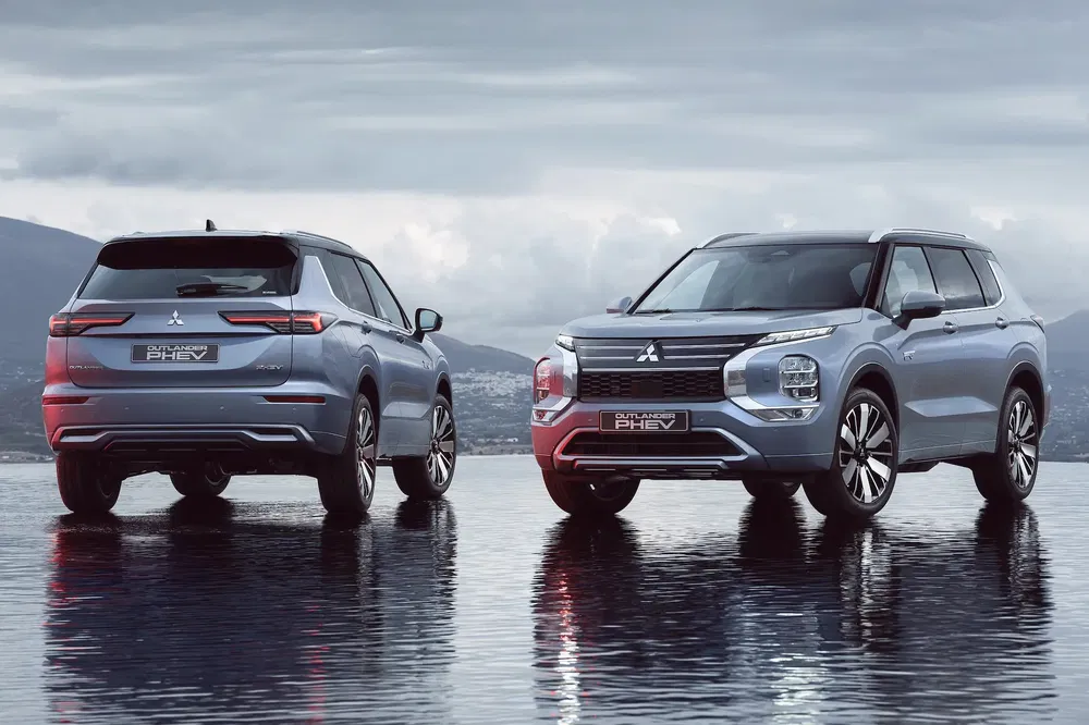 Twee Mitsubishi Outlander PHEV's geparkeerd op een reflecterend oppervlak onder een bewolkte lucht.