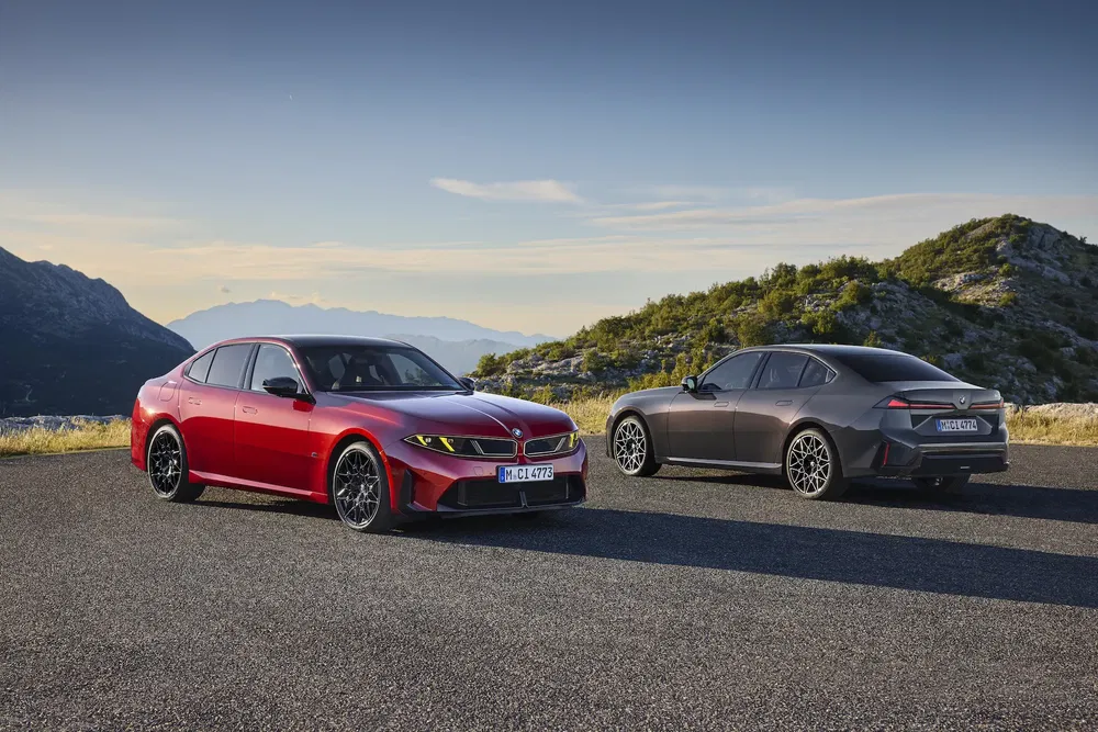 Deux BMW berlines garées sur une route panoramique montagneuse, ciel dégagé.