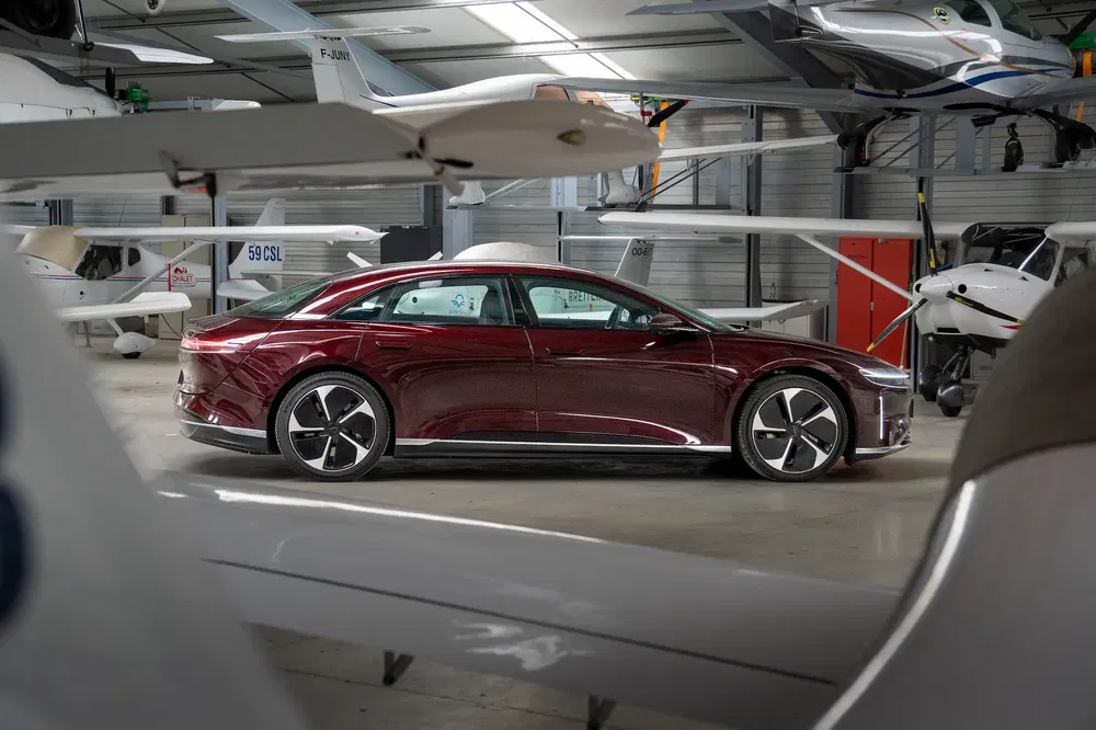 Voiture électrique Lucid Air rouge, garée dans un hangar d'aviation moderne avec des avions légers.